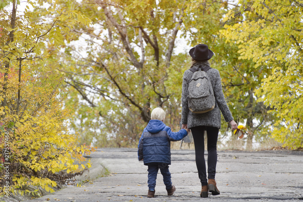 Mom and son are walking in the autumn forest. Back view Mom and son are walking in the autumn forest. Back view