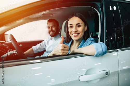 Happy beautiful young couple chooses and buying a new car for the family in the dealership while sitting inside one of car.