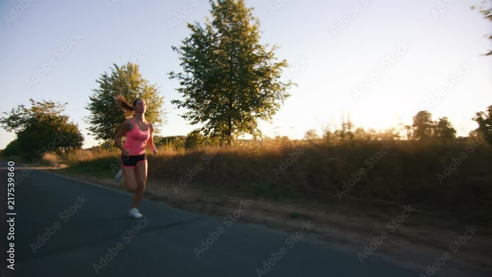 Young sporty girl jogging on a road at sunset in slow-motion Young sporty girl jogging on a road at sunset in slow-motion