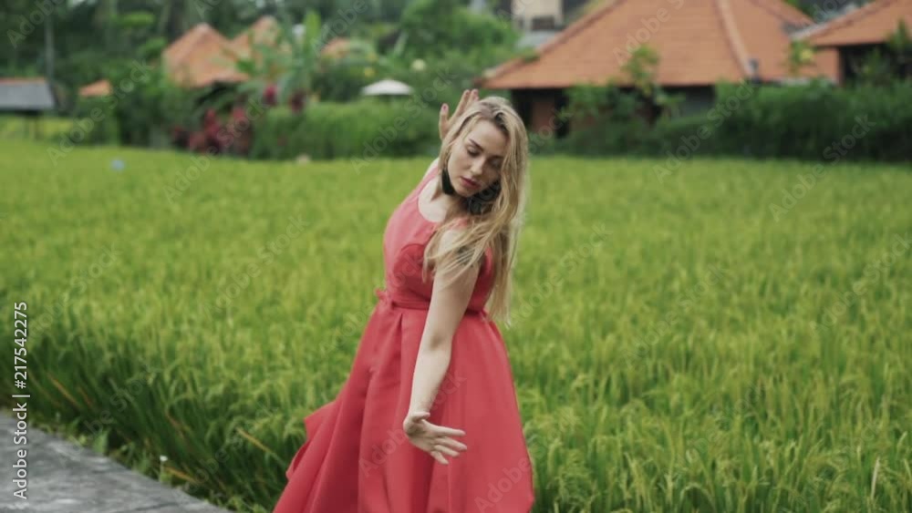 Dance in the slow-motion shooting of a young beautiful girl outside on rice terraces in a red dress with a lush gypsy skirt, against the backdrop of tiled roofs of low houses. Graceful movement of Dance in the slow-motion shooting of a young beautiful girl outside on rice terraces in a red dress with a lush gypsy skirt, against the backdrop of tiled roofs of low houses. Graceful movement of