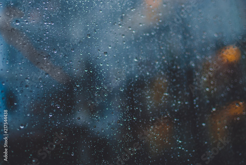 Closeup of raindrops on window glass. Blurred office lights on background. Evening