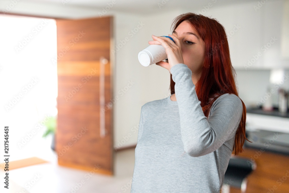 Young redhead girl drinking hot coffee in takeaway paper cup on unfocused background Young redhead girl drinking hot coffee in takeaway paper cup on unfocused background