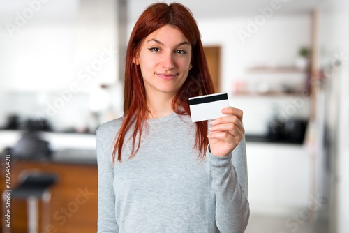 Young redhead girl holding a credit card on unfocused background