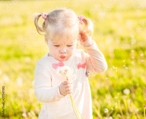 Funny baby girl blowing a dandelion on summer grass © Ermolaev Alexandr