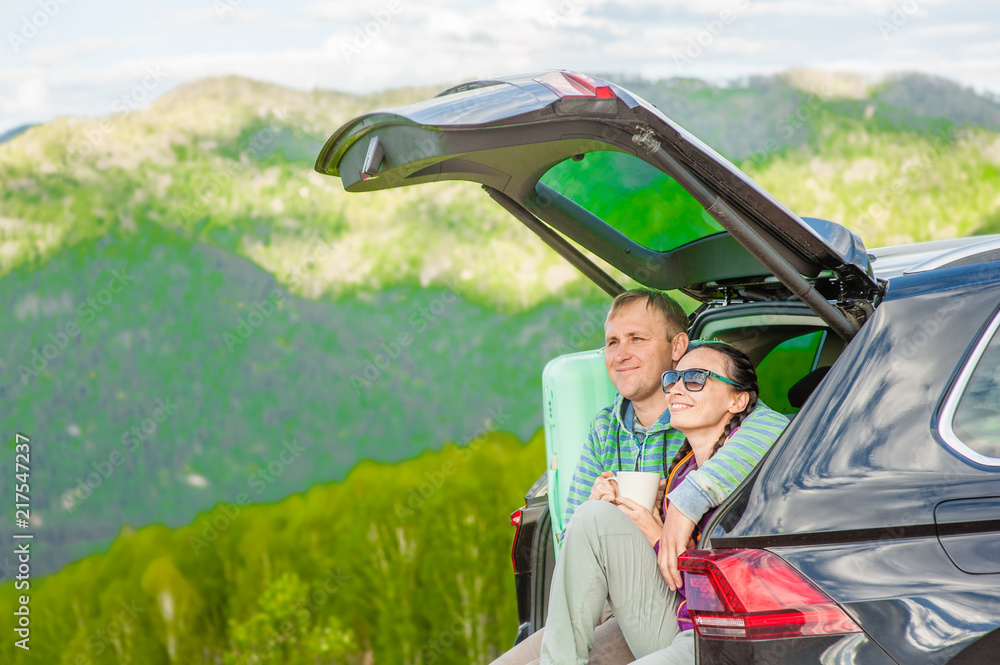 Young couple sitting in hatchback car with mountain background. Space for text
