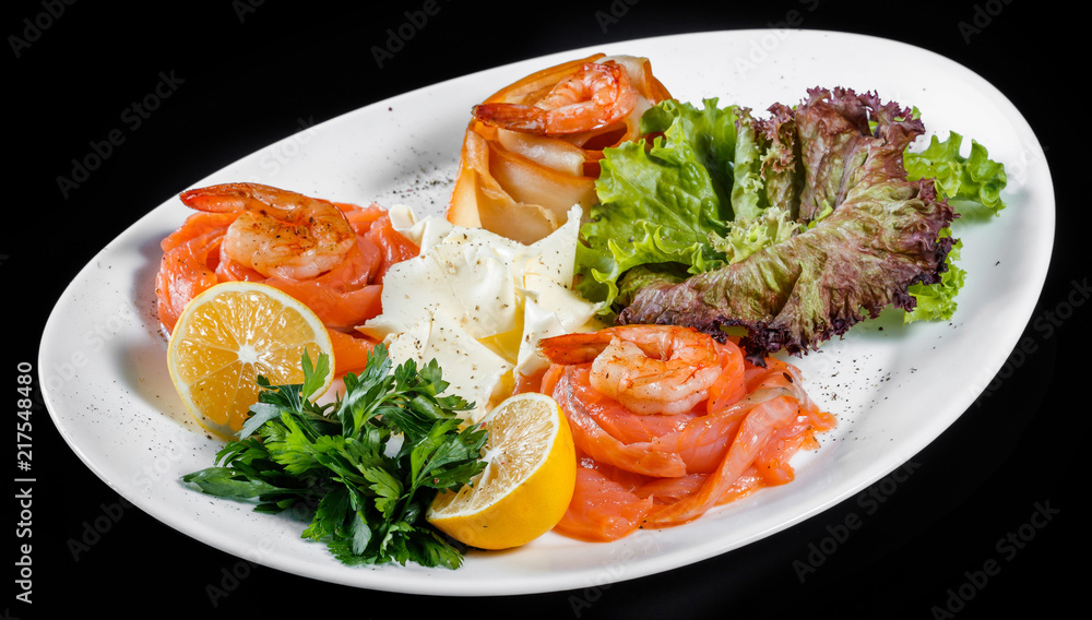 Seafood platter with salmon slice, pangasius fish, shrimp, decorated with lemon and greens on black background isolated Seafood platter with salmon slice, pangasius fish, shrimp, decorated with lemon and greens on black background isolated