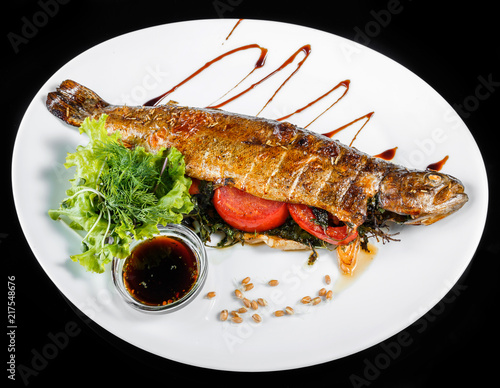 Grilled sea fish with greens and lemon on black background isolated. Healthy food. Top view photo