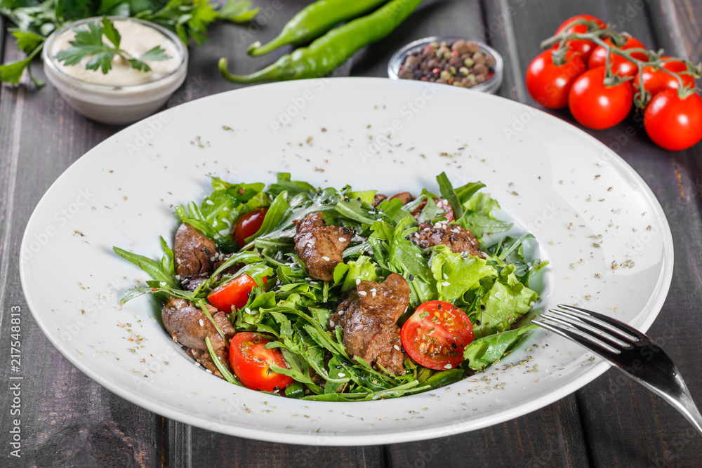 Hot salad with fried liver, cherry tomatoes and mixed greens on dark wooden background. Healthy food. Ingredients on table