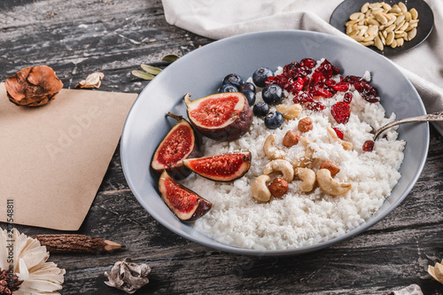 Rice coconut porridge with figs, berries, nuts, dried apricots and coconut milk in plate on rustic wooden background