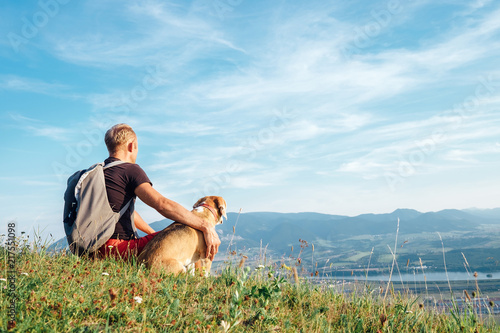 Photography Man with his beagle dog sits on the top of hill over the mountain valley