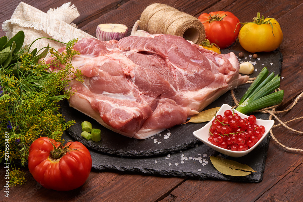 Raw pork meat on a slate stone plate with spices, colorful tomatoes and red currant on a wooden rustic background. Raw pork meat on a slate stone plate with spices, colorful tomatoes and red currant on a wooden rustic background.