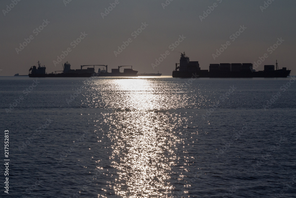 Cargo Ships full of containers lining in front of Thessaloniki port at Sunset into the light. Thessaloniki is one of the main business ports on the Aegean sea