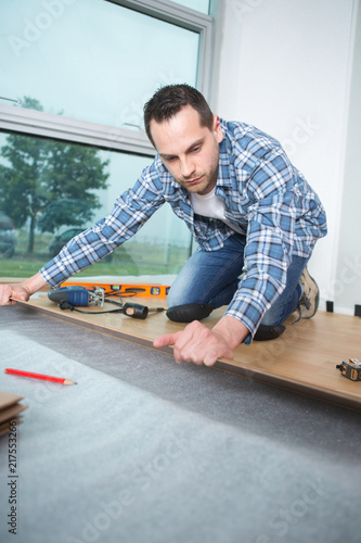 handyman laying down laminate wood flooring boards
