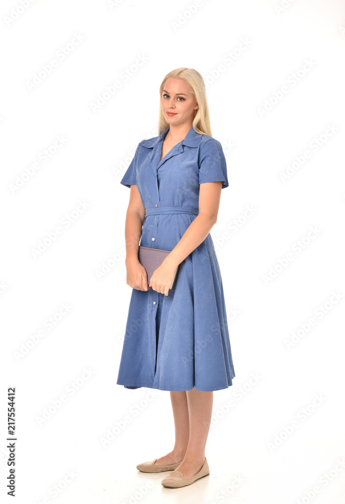 full length portrait of blonde girl wearing blue dress. standing pose holding a book. isolated on white studio background. full length portrait of blonde girl wearing blue dress. standing pose holding a book. isolated on white studio background.