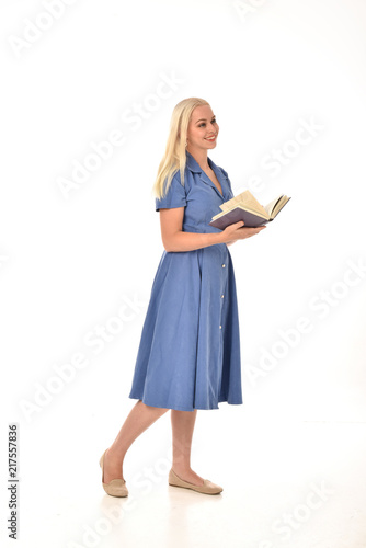full length portrait of blonde girl wearing blue dress. standing pose holding a book. isolated on white  studio background.