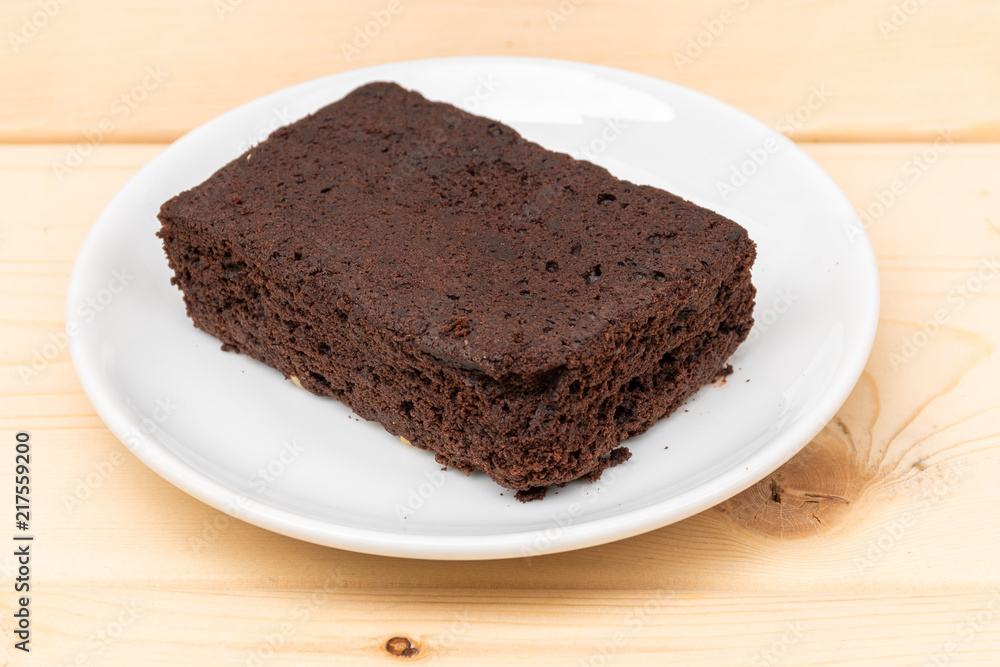 close-up of plain chocolate brownie in white plate on wooden plank