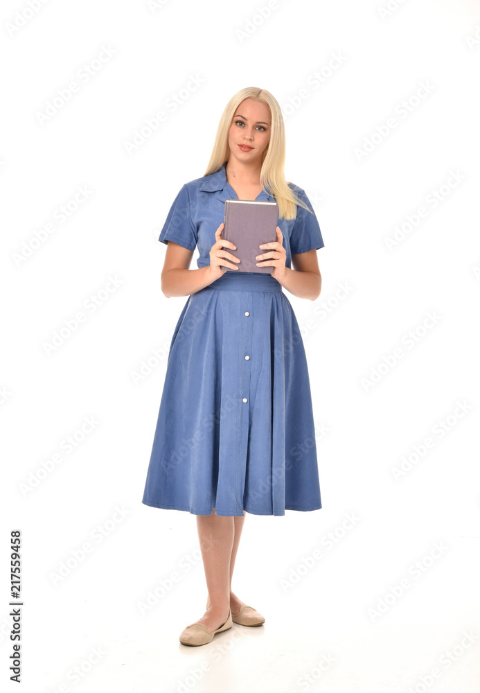 full length portrait of blonde girl wearing blue dress. standing pose holding a book. isolated on white studio background. full length portrait of blonde girl wearing blue dress. standing pose holding a book. isolated on white studio background.