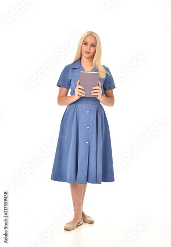 full length portrait of blonde girl wearing blue dress. standing pose holding a book. isolated on white studio background.