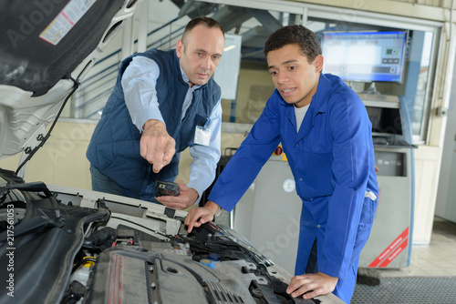 mechanic giving instructions to trainee looking at car engine