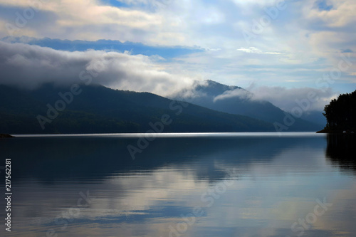 Dawn in the mountains. Morning fog over the sea. Reflection of clouds in the water. Early morning in the mountains. Mirror surface on the water.
