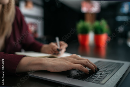 Female designer using laptop, sketching at blank notepad. Woman hand writing in notebook on wooden desk. Concept ease of use of Internet and accessibility of information of working process.