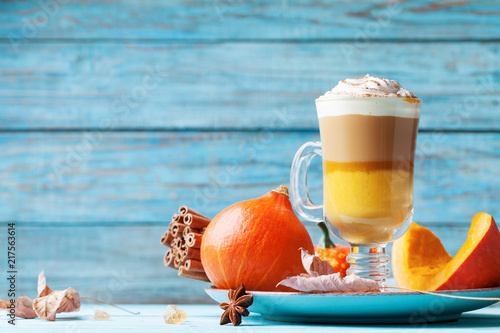 Pumpkin spiced latte or coffee in glass on turquoise wooden table. Autumn, fall or winter hot drink.