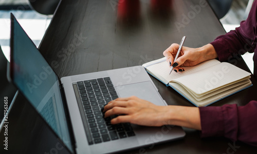 Typing on laptop close up. Young businesswoman sitting at table in coffee shop, look at your notebook screen and ponder business strategy. Girl taking notes in notebook. On table laptop and notebook.