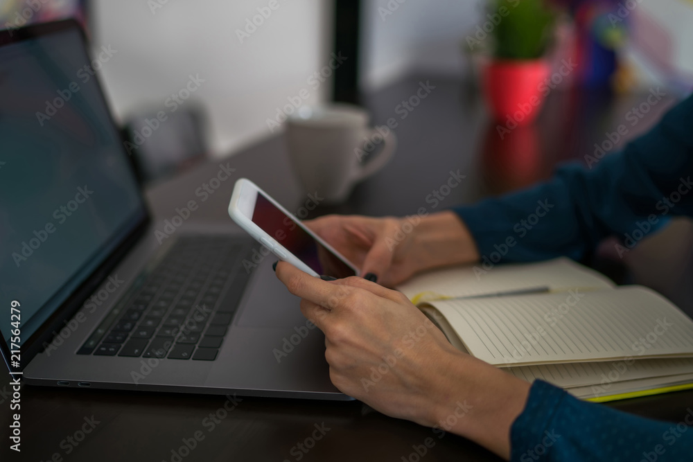 Selective focus on cellphone in hands. Close up view of woman internet user checks notification on mobile phone sitting front laptop computer,female person using modern devices and connecting to netwo Selective focus on cellphone in hands. Close up view of woman internet user checks notification on mobile phone sitting front laptop computer,female person using modern devices and connecting to netwo