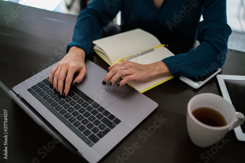 Young woman visits web page by typing search request in network during working at table with cup of herbal tea and paper netbook. New article on own website.