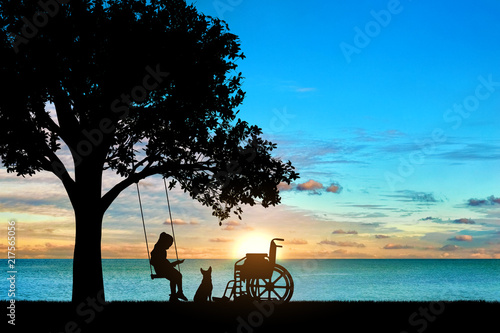 Girl schoolgirl invalid sitting on a swing under a tree by the sea, reading a book, beside a wheelchair and her dog