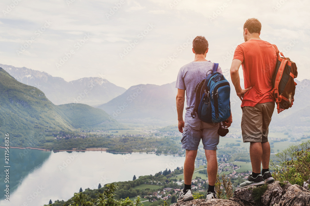friends hiking in Europe, hike in Alps in Annecy, France, outdoor summer activity with backpack, two people backpackers standing on top of mountain and enjoying beautiful nature landscape background friends hiking in Europe, hike in Alps in Annecy, France, outdoor summer activity with backpack, two people backpackers standing on top of mountain and enjoying beautiful nature landscape background
