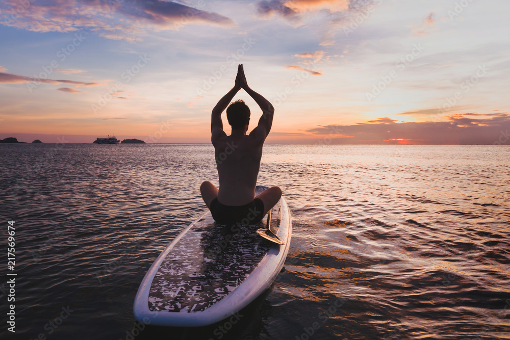 yoga on SUP, silhouette of man sitting in lotus position on stand up paddle board