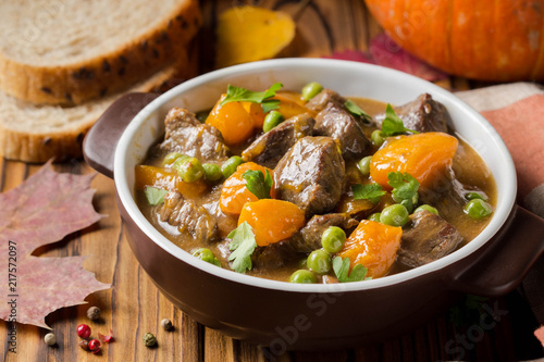 Beef stew with pumpkin, peas and thick sauce, autumn food. Dark bowl on wooden background in rustic style