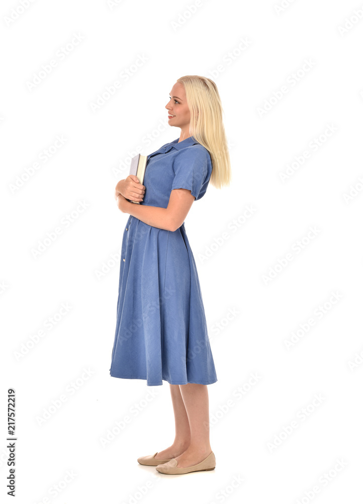 full length portrait of blonde girl wearing blue dress. standing pose holding a book. isolated on white studio background. full length portrait of blonde girl wearing blue dress. standing pose holding a book. isolated on white studio background.