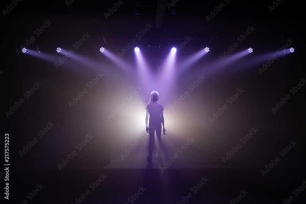 Silhouette eines Mädchens mit Mikrofon auf einer Bühne im Rampenlicht mit Nebel