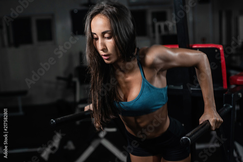 Fitness woman doing push-ups on uneven bars in crossfit gym.