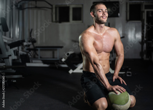 Fitness man poses with a ball in the gym