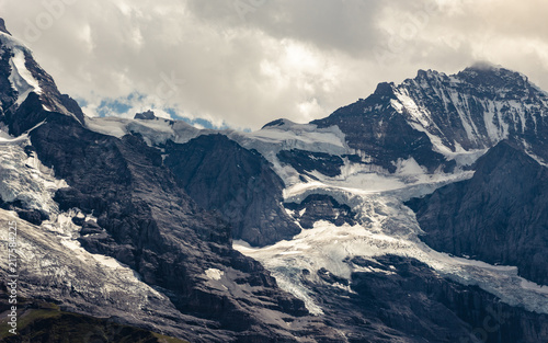 View on Jungfraujoch with Spinx obervatory (3454m / 11.371ft) and the Jungfrau peak (4158m / 13.642ft) under dramatic cloudy sky in summer, Bernese Alps, Switzerland