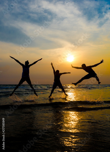 Silhouettes of young group of people jumping on the beach at sunset
