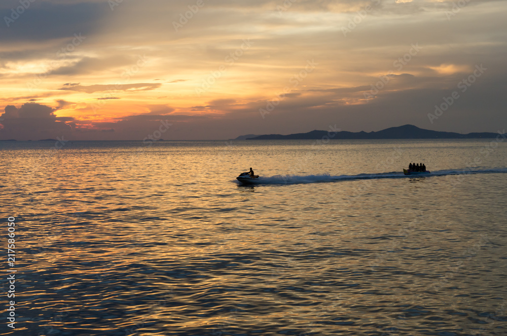 speed boat and banana boat into the sea with sunset