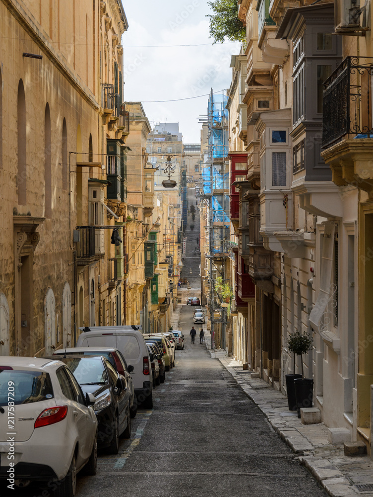 Valetta, Malta - June 2018: Cars and motor scooters parked in the old city, couple walking down the street