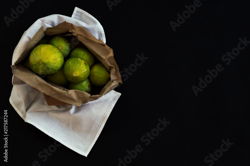 Overhead view of a recycled paper bag with organic fig fruits on unpolluted white fabric. Dark still life scene with black and elegant background. photo