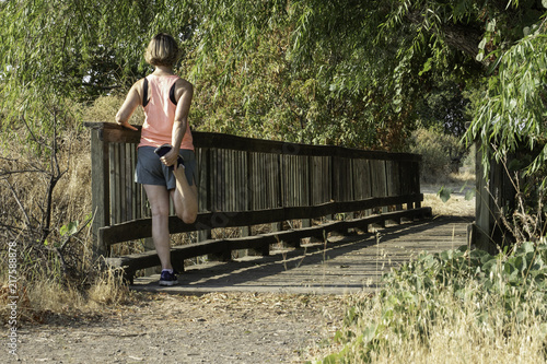 Blonde woman runner doing quad stretch on wooden bridge