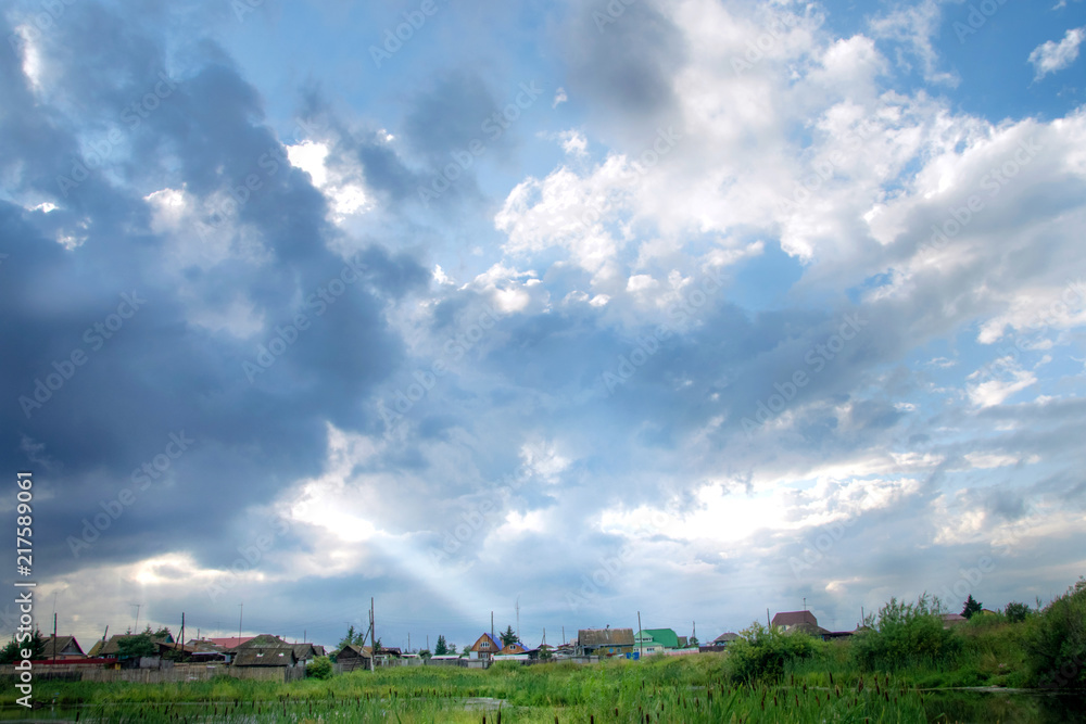Obraz premium rural landscape. The sun's rays make their way through the clouds and Shine on the house after a thunderstorm