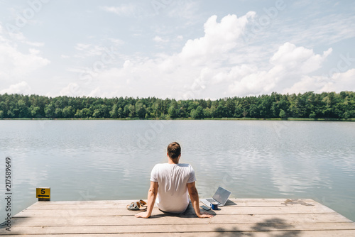 man sitting with laptop and looking on lake. working at vacation. summer time concept