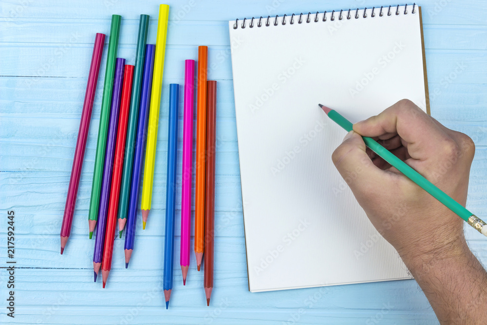 man begins to draw in a notebook for drawing, colored pencils, on a wooden blue background man begins to draw in a notebook for drawing, colored pencils, on a wooden blue background