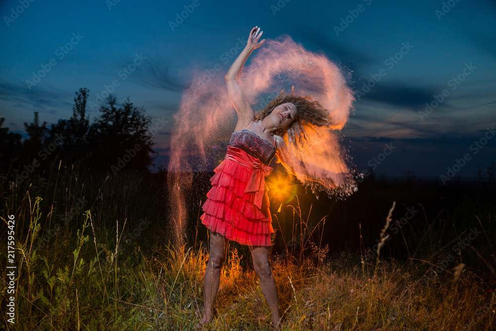 Obraz premium A girl in a black top and red skirt with white cloud arround her hair in a field during photoshoot with flour in sunset