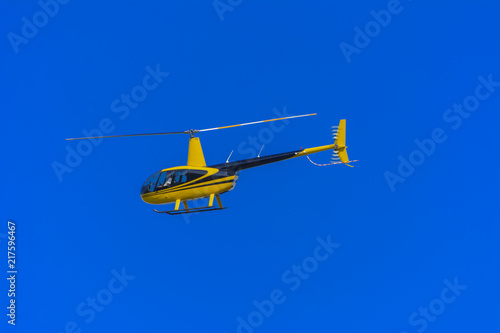 Yellow private helicopter in flight against the background of a bright blue sky with the participation of a crew member, shooting events below. Association with the national flag of Ukraine.