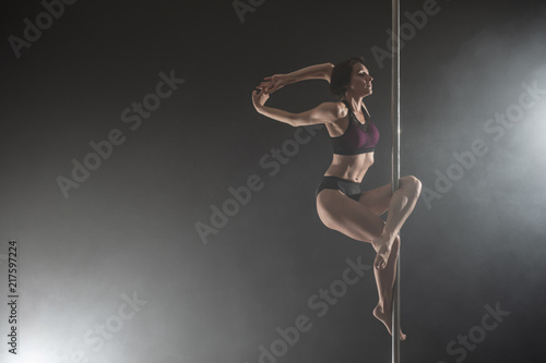 Beautiful slim girl with pylon. Female pole dancer dancing on a black background