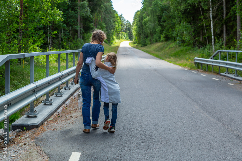 Mor och dotter promenerar på en asfaltsväg genom skogen